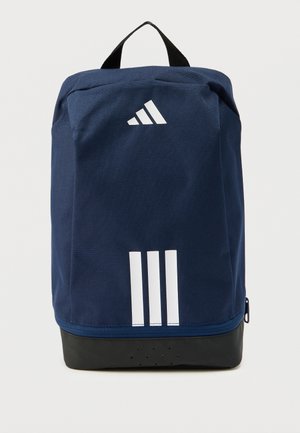 Sac à dos bleu marine en tissu résistant, avec un logo blanc et trois bandes, doté d'un fond noir et d'une poignée supérieure pour le transport.