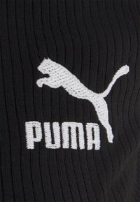Melna ribota auduma, uz kura ir balts izšuvums ar Puma logotipu un lecoša pumā siluetu virs nosaukuma ar treknām, lielajām burtiem.