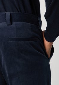 Marina vadmalsbyxor med en mjuk textur, som har en slank midja och en enda bakficka. Tyget visar vertikal ribbning.