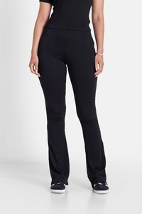 Pantalons en maille texturée noire avec un design évasé, dotés d'une ceinture lisse et associés à des chaussures noires à enfiler.
