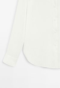 White long-sleeve button-up shirt with a smooth texture, rounded hem, and a single cuff. Features a classic collar and button closures.