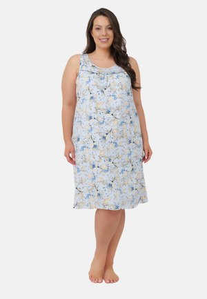 Kobieta stojąca boso, ubrana w sukienkę bez rękawów do kolan z niebiesko-beżowym kwiatowym wzorem.