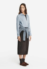 Lyseblå stribet skjorte med knapper og lange ærmer, sort ruskinds nederdel, grå sweater bundet om taljen, mørkebrune mokkasinslippers, ribbede sokker.