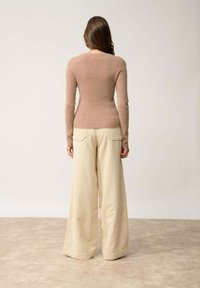 Suéter beige de punto con mangas largas combinado con pantalones de pierna ancha de color crema con rayas verticales y bolsillos traseros.