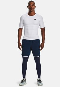 Heren sportoutfit bestaande uit een aansluitend wit T-shirt met korte mouwen, marineblauwe shorts en marineblauwe leggings met witte accenten, ontworpen voor comfort en beweging.