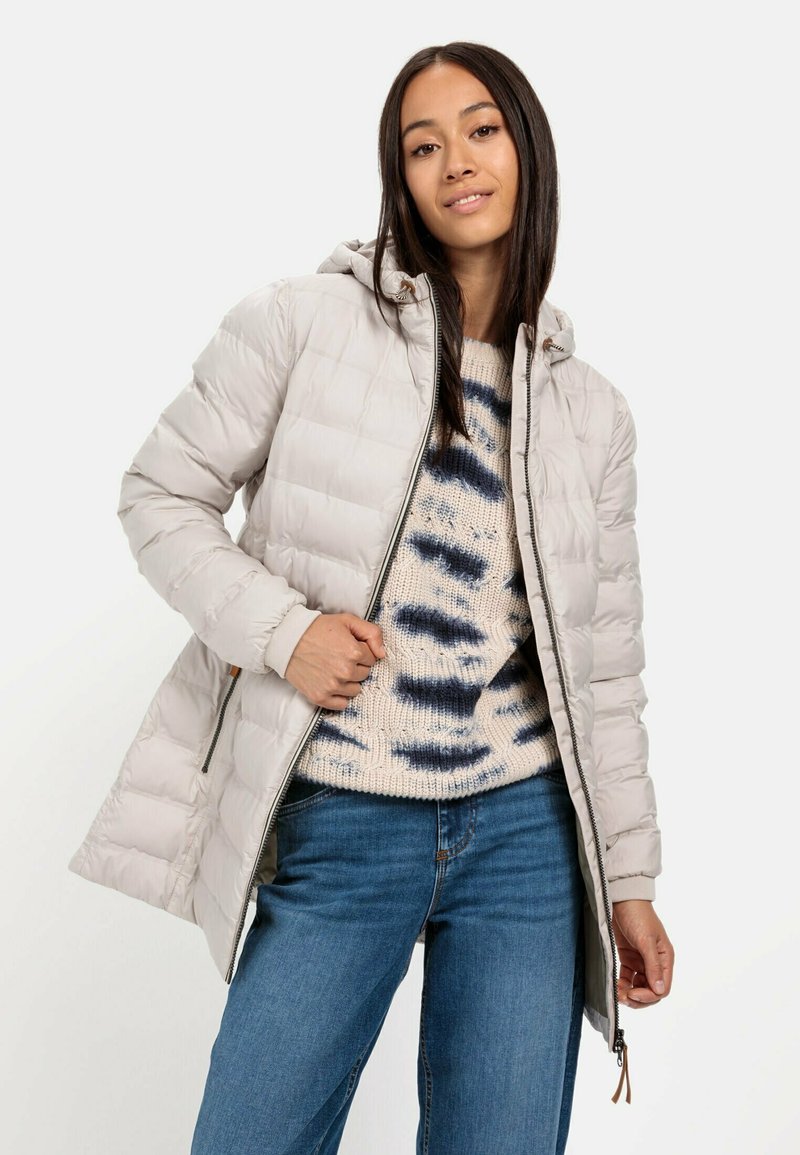 Donzen jas in lichtbeige met een capuchon, met een doorgestikt ontwerp en een rits aan de voorkant. Draag over een crèmekleurige sweater met blauwe patronen en denim jeans.