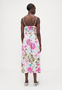 Blumenkleid mit Spaghetti-Trägern, bunten rosa und blauen Blumen auf einem weißen Hintergrund, knielang mit elastischem Taillenbund und einem seitlichen Schlitz.
