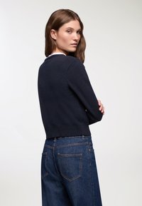Maglione navy a maniche corte in morbido tessuto lavorato a maglia, con scollatura rotonda e orlo a coste. Abbinato a jeans in denim scuro a vita alta.
