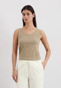 Beige ärmelloses Top aus weichem Material mit runder Ausschnittform und lockerer Passform, kombiniert mit hellcremefarbenen Jogginghosen mit Kordelzug.