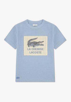 T-shirt en coton bleu clair à manches courtes, avec un motif rectangulaire représentant un crocodile sur un fond rayé jaune.