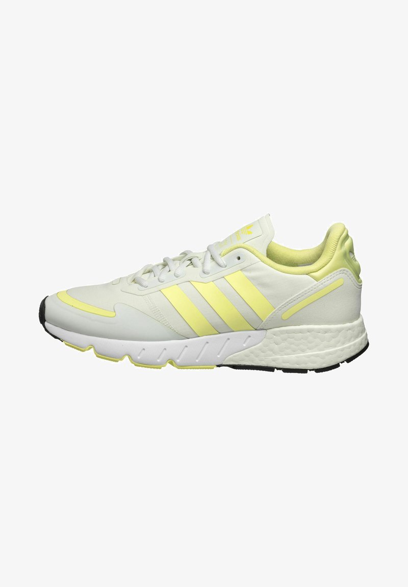 Pantofii sport albi cu accente galbene, având un aspect neted pentru partea superioară, talpă texturată și trei dungi pe lateral pentru branding.