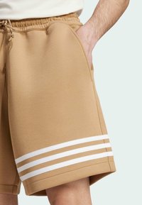 Tan cotton shorts with a relaxed fit, featuring white triple stripe accents on the hem and side pockets. Soft texture and elastic waistband.