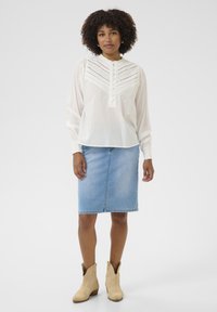 Blusa blanca de manga larga con detalles de encaje, con botonera, combinada con una falda lápiz de mezclilla azul claro y botas de vaquero beige.