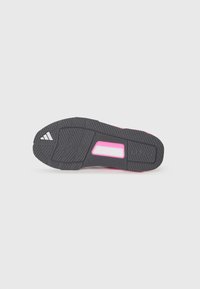 Suola di scarpa in gomma nera con impugnature testurizzate, caratterizzata da un accento rosa e dalla parola "TRAXION" in rilievo. Logo triangolare in un angolo.