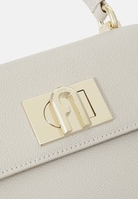 Vaaleanharmaa nahkainen käsilaukku, jossa on kultasävyinen metallinen solki, johon on painettu logo, teksturoitu pinta ja siistit tikkausreunat.