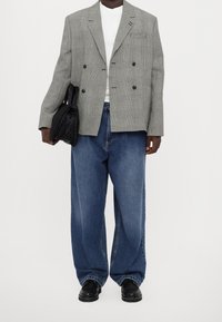 Szary w kratę dwurzędowy żakiet, biały T-shirt, luźne niebieskie dżinsy i czarne buty. Czarna torba trzymana pod lewą ręką.