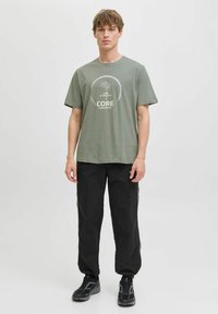 Camiseta de cuello redondo en color verde oliva con estampado gráfico, combinada con pantalones holgados negros. Ambos artículos tienen una textura suave y un diseño cómodo.