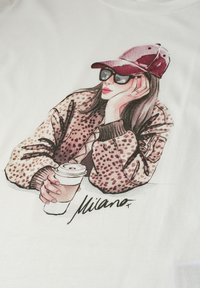 Femme portant une casquette rouge, des lunettes de soleil et une veste à imprimé léopard, tenant une tasse de café, avec "Milano" écrit en dessous.