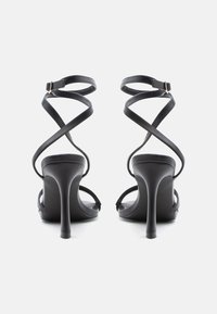 Mustad kõrge kontsaga sandaalid risti üle käivate rihmadega, pahkluu pandlaga ja elegantse kontsaga. Siledapintseline ja minimalistliku disainiga.