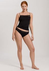 Camiseta de algodón negra con tirantes finos, adornada con un borde de encaje, combinada con un bikini negro con dobladillo de encaje a juego. Textura suave.