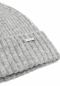 Szara dzianinowa czapka z prążkowanym wzorem i teksturowanym wykończeniem, z małą metalową metką przyszytą z boku. Materiał wydaje się miękki i ciepły.