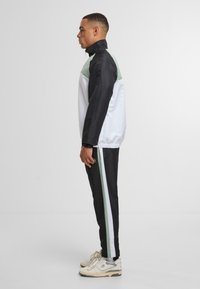 Jacka och byxor i svart, vitt och ljusgrönt. Jackan har hög krage och elastiska muddar. Byxorna har vita och gröna sidostråk.