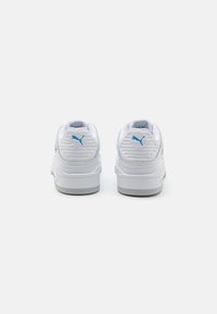 Baskets de sport blanches avec un design texturé, des accents bleus et une semelle épaisse. La vue arrière montre des détails nervurés et le placement du logo.