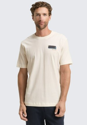 Crème-kleurig katoenen t-shirt met korte mouwen, met een rechthoekige blauw-zwarte grafiek op het linkerborstgebied.