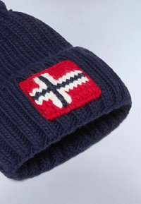 Marineblauwe gebreide beanie met een geribbelde textuur, voorzien van een rechthoekige rode patch met een geborduurd ontwerp van een wit en blauw kruis.