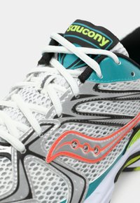 Dettaglio ravvicinato di una scarpa da corsa grigia Saucony con lacci bianchi, accenti in teal e arancione, tomaia in mesh traspirante e logo del marchio sulla linguetta e sul lato.