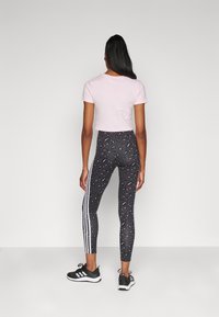 Cropped pink t-shirt paired with black leggings featuring a leopard pattern and white side stripes, worn with black athletic shoes.