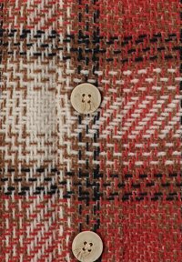 Woven tkanina s rdečim, rjavim in belim karo vzorcem; na sprednji strani ima svetlo obarvan gumb s štirimi luknjami za zapenjanje.