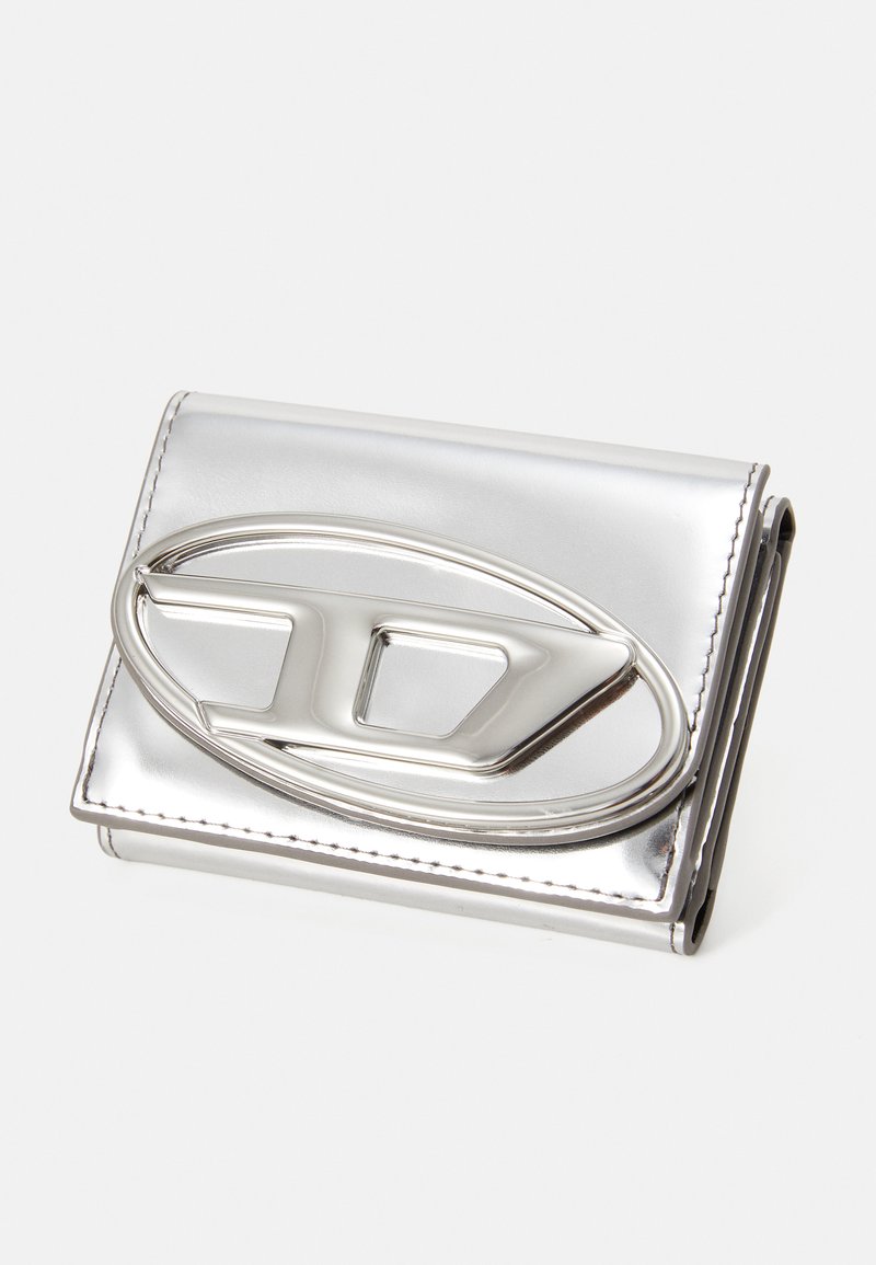 Silbermetallic Geldbörse mit einem auffälligen ovalen Logo. Glatte Textur, Klappdesign und sichtbare Nähdetails. Kompakte Form.