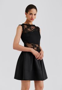 Čierne šaty s priliehavým čipkovaným živôtikom s kvetinovými vzormi, s oblým výstrihom a rozšírenou saténovou sukňou pre väčší objem.