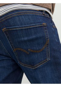 Tmavě modré džíny z denimu mají zadní kapsu se žlutým prošitím a zakřiveným designem. Měkká tkanina s hladkou texturou a přizpůsobeným střihem.