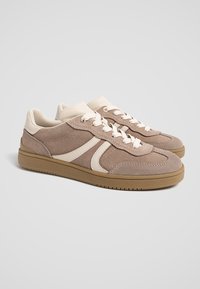 Sneaker aus hellbraunem Wildleder mit cremefarbenen Akzenten. Verfügt über eine abgerundete Form, Schnürung und eine strukturierte Gummisohle. Lässiges Design.