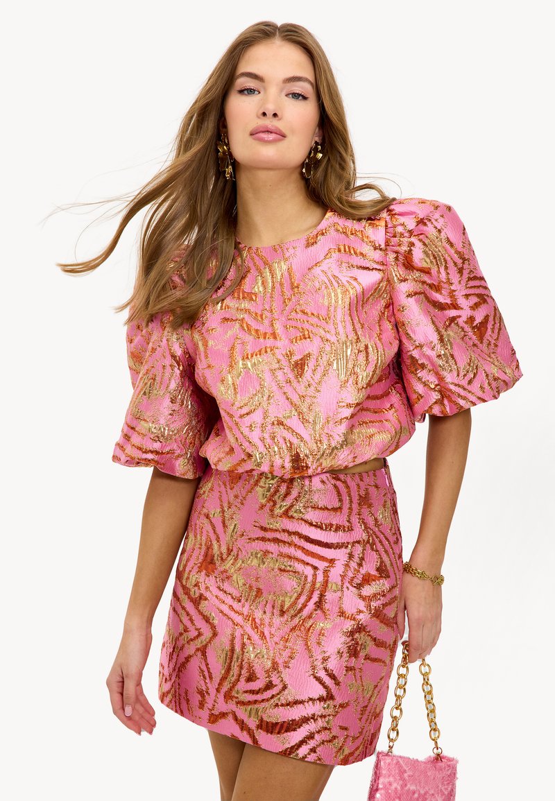 Vestido rosa con patrón abstracto dorado, mangas cortas abullonadas y falda ajustada. Tejido texturizado y un bolso mini a juego con cadena.