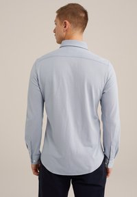 Camisa de manga larga azul claro con cuello clásico, puños abotonados y una textura a rayas sutil, presentando un dobladillo curvado y detalle en el yoke trasero.