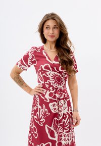 Rotes und beiges gemustertes Wickelkleid mit kurzen Ärmeln, das florale und abstrakte Designs aufweist und mit einem Stoffgürtel in der Taille gebunden ist.