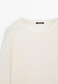 Pull à manches longues couleur crème, col rond, fabriqué en tissu tricoté doux et léger, avec une étiquette de marque noire à l'intérieur du col.