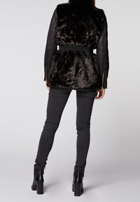 Czarna kurtka z sztucznego futra z dopasowaną talią i skórzanymi rękawami, w połączeniu z wąskimi czarnymi dżinsami i botkami na grubym obcasie.