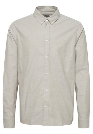 Svetlo béžová košeľa s dlhým rukávom a golierom na gombíky, prednými gombíkmi a hladkým povrchom. Má klasický strih a manžety s gombíkmi.