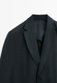 Tmavě šedé sako na míru s výstřihem s zářezy, uzavíráním na jeden knoflík a hladkou vnitřní podšívkou, zobrazené na bílém pozadí.