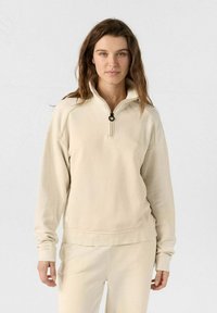 Beige zip-up sweatshirt met hoge kraag, voorzien van een ronde ritsen trekker, geribbelde manchetten en een losse pasvorm. Zachte stoftextuur.