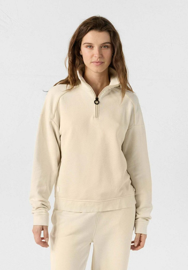 Beige zip-up sweatshirt met hoge kraag, voorzien van een ronde ritsen trekker, geribbelde manchetten en een losse pasvorm. Zachte stoftextuur.