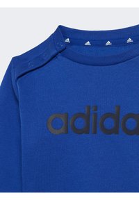 Felpa in cotone blu con collo a costine, bottoni a pressione sulla spalla e grande logo "adidas" stampato sul davanti.