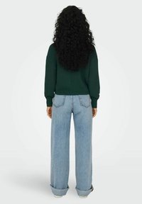 Maglione verde a maglia con una vestibilità rilassata, abbinato a jeans a gamba larga blu chiaro. I jeans hanno orli arrotolati e tasche posteriori.