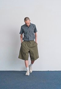 Pasiasta koszula z krótkim rękawem w czarno-białe paski, zestawiona z luźnymi oliwkowymi szortami i białymi sneakersami. Prosty design o luźnym kroju.