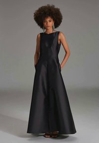 Black satin sleeveless gown with a fitted top, flared skirt, and side pockets. Smooth texture, minimalistic design, floor-length.