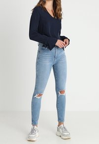 Námořnická halenka s dlouhým rukávem a zvonovými manžetami, zkombinovaná se světle modrými roztrhanými skinny džíny a bílými teniskami. Minimalistický, příležitostný outfit.